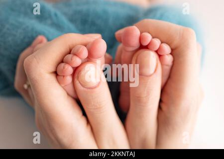 La madre sta facendo il massaggio sul suo piede del bambino. I piedi del bambino nelle mani della madre su un blu. Foto Stock