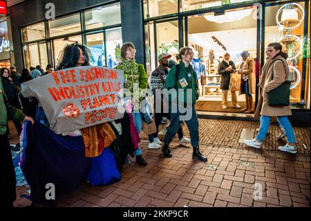 Amsterdam, Paesi Bassi. 25th Nov 2022. Gli acquirenti guardano gli attivisti della XR marciare per le strade durante una marcia dimostrativa contro l'industria della moda. L'organizzazione climatica, Extinction Rebellion (XR) ha organizzato una dimostrazione contro il consumo eccessivo durante il Black Friday, e per porre fine a questa giornata. Gli attivisti hanno svolto un'azione chiamata Free (ky) Friday in Piazza Dam, dove hanno messo centinaia di vestiti di seconda mano che le persone potrebbero portare per libero o scambiare vestiti. Con questa azione l'organizzazione desidera mettere il profitto sopra la gente ed il pianeta e rompere con il cul del consumatore Foto Stock