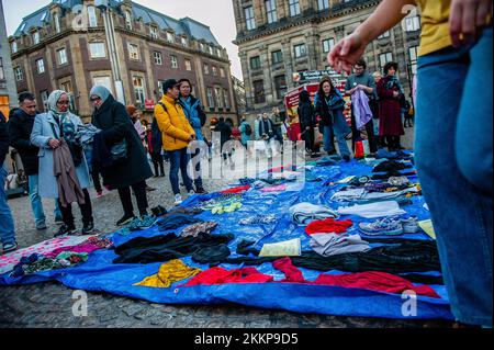 Amsterdam, Paesi Bassi. 25th Nov 2022. La gente guarda i vestiti liberi di seconda mano posti sul terreno per libero durante una dimostrazione di ribellione di estinzione. L'organizzazione climatica, Extinction Rebellion (XR) ha organizzato una dimostrazione contro il consumo eccessivo durante il Black Friday, e per porre fine a questa giornata. Gli attivisti hanno svolto un'azione chiamata Free (ky) Friday in Piazza Dam, dove hanno messo centinaia di vestiti di seconda mano che le persone potrebbero portare per libero o scambiare vestiti. Con questa azione l'organizzazione desidera mettere il profitto sopra la gente ed il pianeta e rompere con Foto Stock