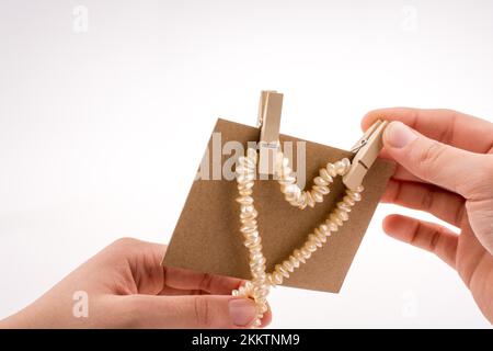 Collana di perle costituisce forma di cuore su carta su sfondo bianco Foto Stock