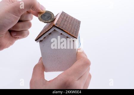 Mano moneta caduta nel salvadanaio a forma di un modello di casa Foto Stock