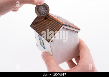 Mano moneta caduta nel salvadanaio a forma di un modello di casa Foto Stock