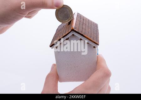 Mano moneta caduta nel salvadanaio a forma di un modello di casa Foto Stock