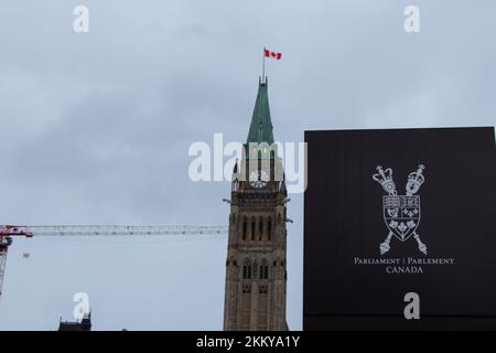 Un segno per e il logo del Parlamento del Canada è visto con Parliament Hill, Peace Tower sullo sfondo in una giornata nuvolosa a Ottawa. Foto Stock