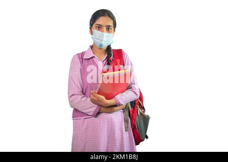 Ritratto di una bambina che indossa una maschera protettiva con borsa e notebook Foto Stock