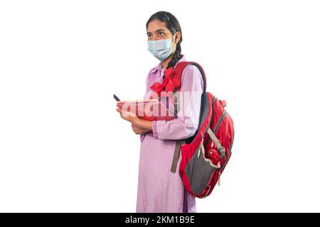 Ritratto di una bambina che indossa una maschera protettiva con borsa e notebook Foto Stock