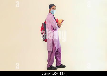 Ritratto di una bambina che indossa una maschera protettiva con borsa e notebook Foto Stock