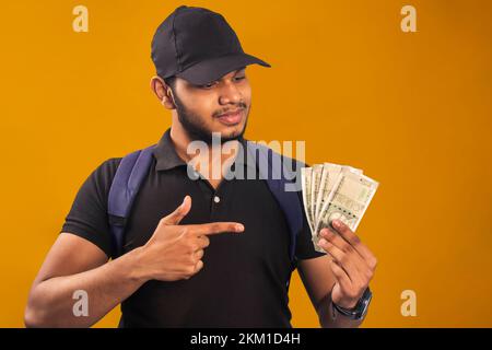 Giovane uomo di consegna che tiene le banconote della rupia indiana sorridente felice indicando con la mano e il dito Foto Stock