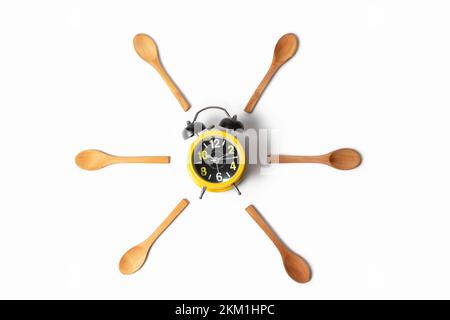 Vista dall'alto della sveglia gialla con cucchiai di legno intorno isolato su sfondo bianco Foto Stock