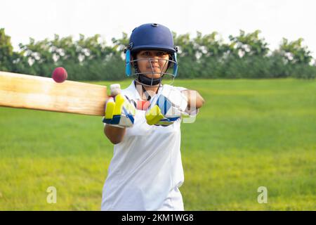 Giocatore di cricket femminile che indossa un equipaggiamento protettivo e colpisce il pallone con un pipistrello sul campo Foto Stock