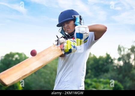 Giocatore di cricket femminile che indossa un equipaggiamento protettivo e colpisce il pallone con un pipistrello sul campo Foto Stock