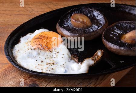 Uova fritte e funghi a fette cucinate in una rustica padella di ghisa nera. Colazione salutare o brunch fotografia, primo piano sopra la testa. Foto Stock