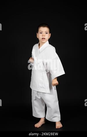 Un ragazzino pratica arti marziali, lezioni di karate in kimono su sfondo nero Foto Stock