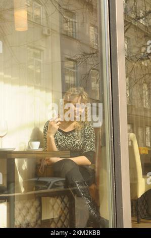Giovane donna seduta al tavolo nel ristorante bevendo vino dietro la finestra di vetro. Kiev, Ucraina Foto Stock