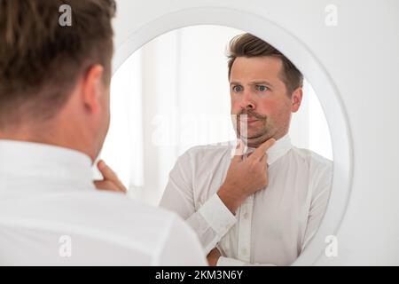 giovane con un doppio mento che ne esamina il riflesso in specchio Foto Stock