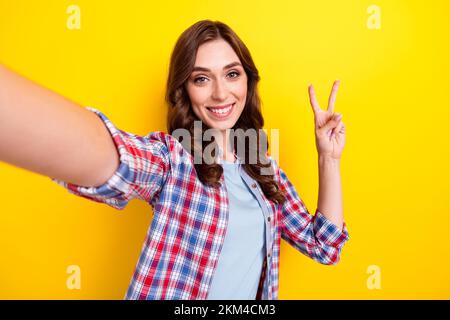 Primo piano selfie cadre di giovane allegro adorabile donna indossare camicia a quadri mostrando v-segno hi abbonati online flusso isolato su sfondo giallo colore Foto Stock