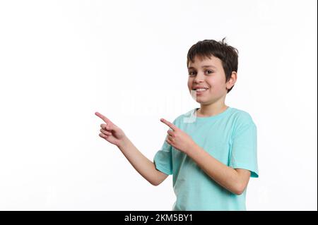 Ritratto su sfondo bianco di ragazzo di scuola intelligente, sorrisi che ti guarda, punti a spazio pubblicitario per la tua promozione Foto Stock