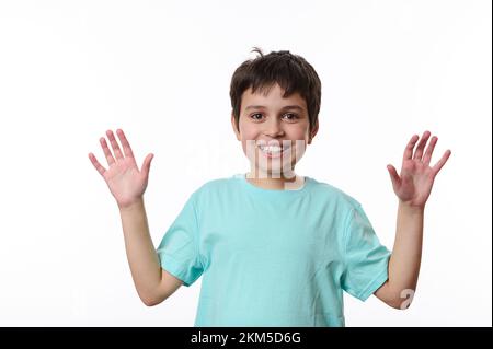 Adorabile ragazzo presiede mostra le mani palme alla macchina fotografica e sorride con bel sorriso toothy, isolato su sfondo bianco Foto Stock