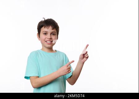 Adorabile bambino preseen sorridente, ragazzo di età scolastica che ti guarda e che indica lo spazio per la pubblicità su sfondo bianco Foto Stock