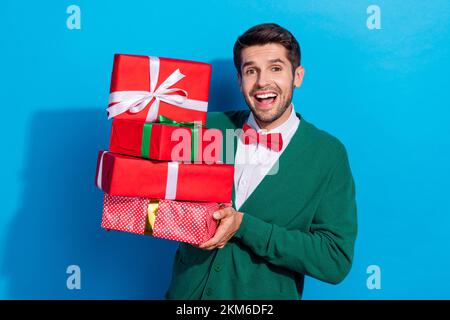 Foto del tipo eccitato positivo vestito xmas verde cardigan ascendente regali pila isolato di colore blu sfondo Foto Stock