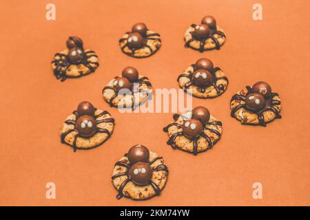 Trick o trattare i biscotti ragno di Halloween con ragni di cioccolato creepy strisciando su biscotti croccanti appena sfornati su sfondo arancione Foto Stock