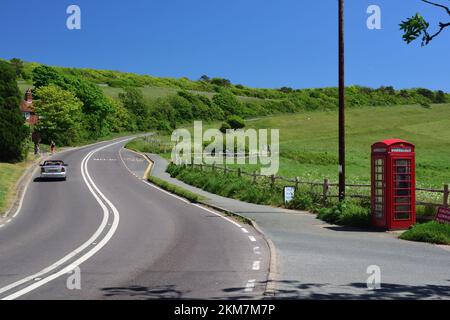 Un'iconica cassetta telefonica rossa accanto a una strada principale con due linee bianche, in un ambiente rurale. Foto Stock