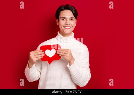 Ritratto di ragazzo brunetto ottimista bello indossare maglia jumper tenere carta come blogging promo instagram account isolato su sfondo di colore rosso Foto Stock