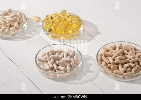 integratore alimentare in capsule in capsule di petri su tavolo di legno bianco. omega 3 e varie pillole di vitamine per il cuore e il supporto del sistema vascolare Foto Stock