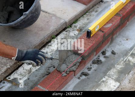 Lavori di costruzione in corso. Costruttore maschile che lavora con mattoni rossi. Foto ravvicinata della parete in muratura. Foto Stock