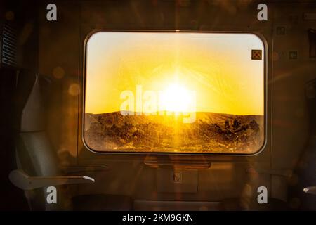 Interno di un treno passeggeri con vista dalla finestra del sole sull'orizzonte del paesaggio Foto Stock