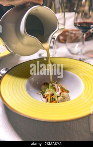 Lo chef versa la zuppa nel piatto sul tavolo per una cena di lusso. Foto Stock