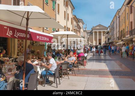 Bardolino città Italia, vista in estate delle persone che si rilassano ai tavoli da caffè in Via San Martino, nel centro storico di Bardolino, Lago di Garda Foto Stock