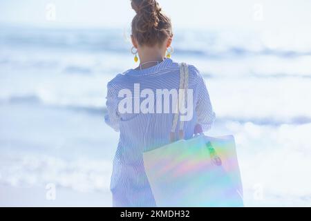 Vista da dietro donna di mezza età con sacco di paglia bianca in spiaggia. Foto Stock