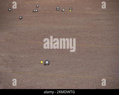 Palline di petanque metalliche e un piccolo jack giallo su un campo di sabbia Foto Stock