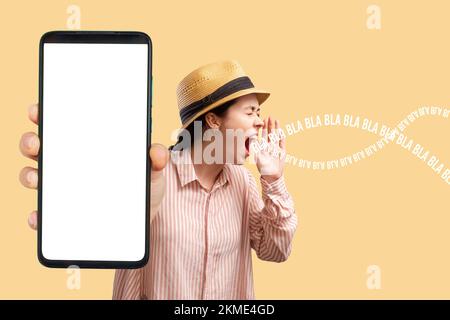 Pubblicità e app per smartphone. Una giovane donna caucasica in un cappello di paglia mostra un primo piano di un telefono con uno schermo bianco e grida a qualcuno. Beffa Foto Stock