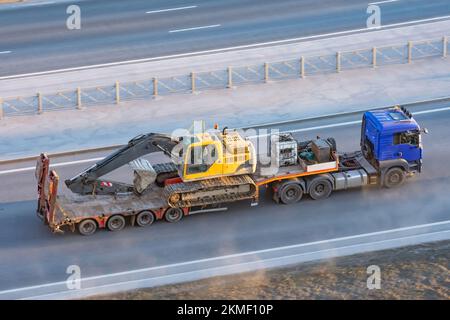 Autocarro con piattaforma rimorchio lunga per il trasporto di macchinari pesanti, escavatore cingolato carico con benna. Trasporto su autostrada Foto Stock