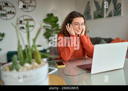 Giovane donna in cuffia che usa il notebook per guardare il webinar elearning a casa. Foto Stock