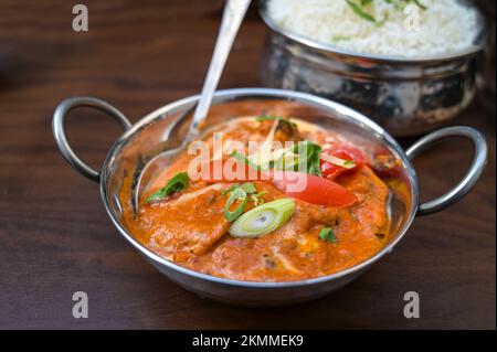 Piatto di curry indiano con pomodoro e porro in una ciotola d'argento servito con riso su un tavolo di legno marrone scuro, spazio copia, fuoco selezionato, profondità stretta di fuoco Foto Stock