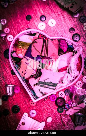 Cucito rosa still-life su un cuore a forma di cestello di sarto bottoni e filo di amore designer Foto Stock