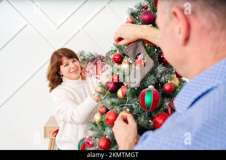 Sorridente felice coppia di mezza età che decora l'albero di natale a casa. Coppia felice insieme a casa, concetto di natale Foto Stock
