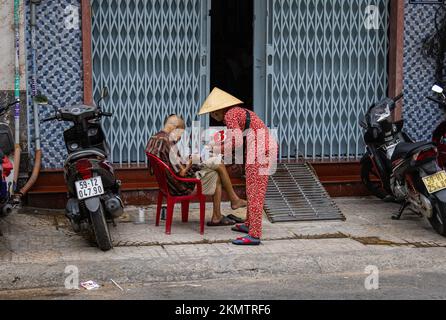 Ho Chi Minh City, Vietnam - 8 novembre 2022: Donna anziana in abiti vietnamiti tradizionali e non la headdress vende biglietti della lotteria a un vecchio o Foto Stock