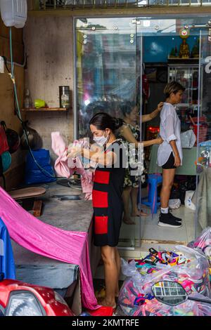 Ho Chi Minh City, Vietnam - 8 novembre 2022: In un piccolo negozio di sarto a Saigon. Una donna ferra il tessuto prima che venga trasformato in un abito Ao dai. Una piccola t Foto Stock