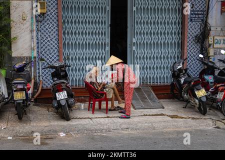 Ho Chi Minh City, Vietnam - 8 novembre 2022: Donna anziana in abiti vietnamiti tradizionali e non la headdress vende biglietti della lotteria a un vecchio o Foto Stock