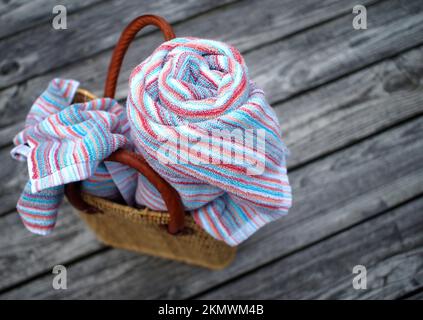 Per una giornata in spiaggia - tote da spiaggia in tessuto con fasce in pelle; con teli da spiaggia colorati, uno arrotolato, uno sciolto, su ruvido, rustico, weathe Foto Stock