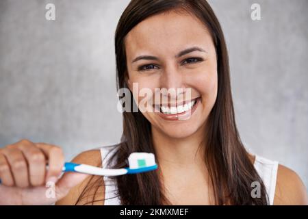 Il suo segreto per un bel sorriso. Un ritratto isolato di una giovane donna che si sfrega felicemente i denti. Foto Stock