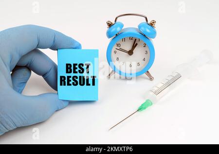 Concetto di medicina. Sul tavolo c'è una siringa e una sveglia, in mano un taccuino con l'iscrizione - MIGLIOR RISULTATO Foto Stock