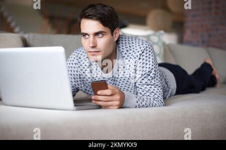 Quel momento in cui non sai cosa inviare un SMS... un uomo che usa il suo telefono cellulare e il suo computer portatile mentre ha un momento premuroso. Foto Stock