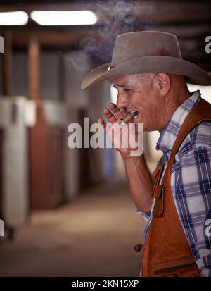 Sapori come l'Occidente. un cowboy anziano che gode un sigaro sul suo ranch. Foto Stock