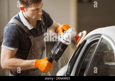 Dettaglio auto - l'operaio maschile tiene una lucidatrice in mano e lucida l'auto bianca in negozio di riparazione auto. Foto Stock