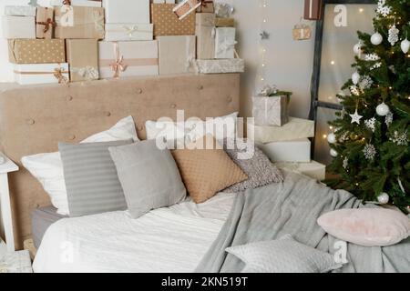 Pila di regali di Natale in colorato involucro con nastri contro una parete bianca con stelle d'argento. Albero di Natale in camera. Foto Stock